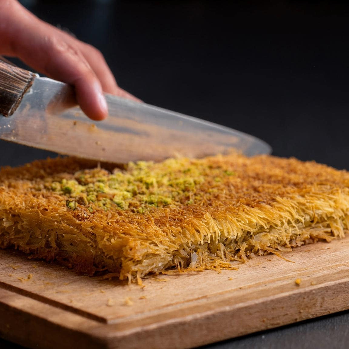 Person cutting a square of pastry on a wooden board with a knife.